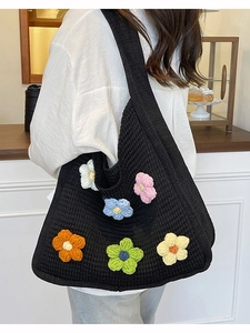 Black knit tote bag with 3D colorful crochet flowers shown on model in a cozy cafe setting