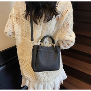 Close-up of black lychee grain leather bucket bag with gold handle and metal feet