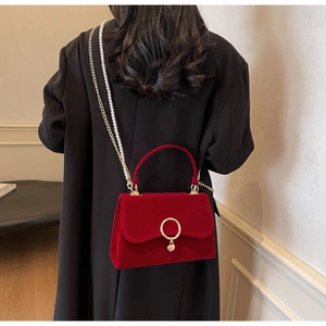 Detail of red velvet crossbody bag with gold heart pendant and pearl chain strap