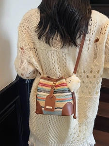 Colorful striped woven bucket bag with brown strap and white plush ball charm on model