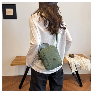 Rear view of a model wearing a green nylon multi-pocket crossbody bag in a minimalist room