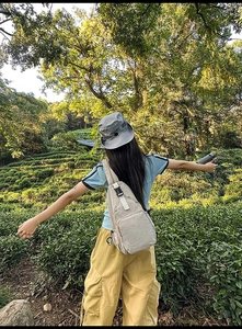 Outdoor view of a beige nylon crossbody bag worn by a model in a sunny tea plantation