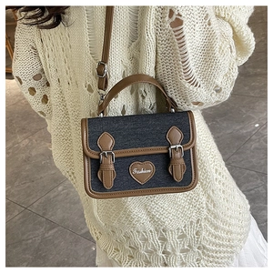 Close-up of denim crossbody bag with brown leather trim and heart logo on white sweater