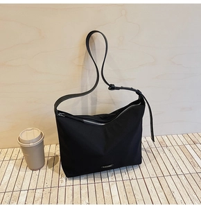 Detail showing black nylon shoulder bag with adjustable strap and metal logo plate