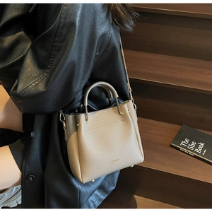 Close-up of beige litchi grain leather texture and gold metal accents on a stylish handbag