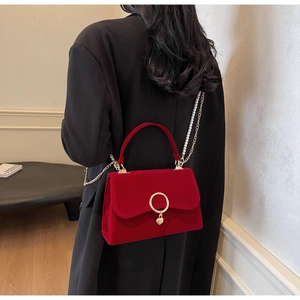 Detail of red velvet handbag featuring gold circular lock and elegant pearl chain strap