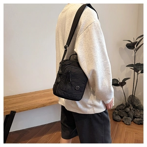 Detail of black nylon multi-pocket crossbody bag with adjustable strap and metal logo