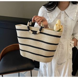 Detail of hand-woven beige straw tote bag with black stripes and circular woven handles