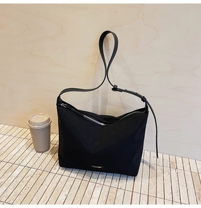 Detail of a minimalist black nylon shoulder bag featuring a silver zipper and metal logo tag