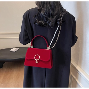 Detail of red velvet handbag with heart pendant, pearl chain strap and gold hardware