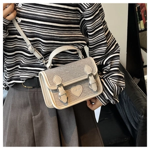 Detail of grey denim mini crossbody bag with heart patch and leather trim worn by a model