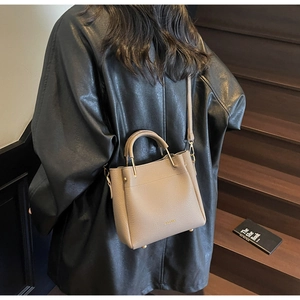 Close-up of beige litchi grain leather bucket bag with SOLOMON branding on stairs