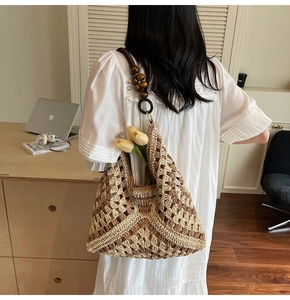 Detail of woven straw tote bag with contrast stitching and dark beaded shoulder strap