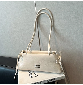 Détail du sac baguette crème avec logo métallique et nœuds de serrage sur les côtés