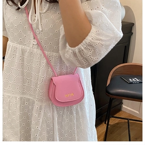 Pink mini crossbody saddle bag with golden lettering shown in a casual lifestyle setting