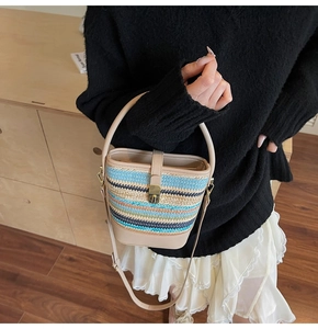 Detail view of woven straw bucket bag with blue stripes and elegant leather handle