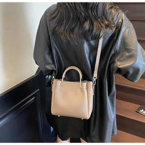 Model wearing a khaki grey pebble leather bucket bag with top handles and shoulder strap