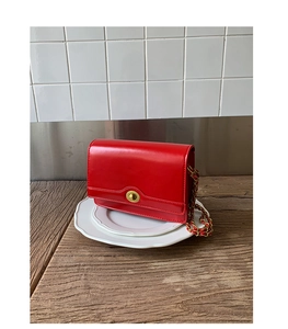 Detail of red glossy leather crossbody bag featuring a golden rotary lock and chain strap