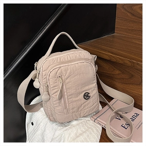 Detailed view of pale pink nylon crossbody bag with multiple zippers on wooden steps