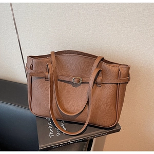 Detail of brown litchi pattern leather tote bag with gold buckle on an elegant book