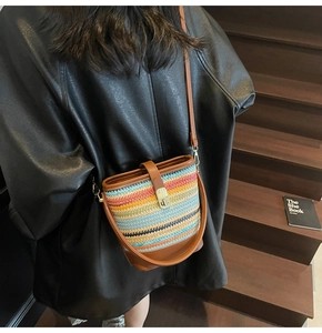 Detail of colorful striped straw bucket bag with brown leather trim and metal lock closure