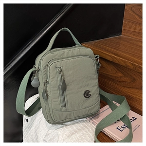 Sage green nylon crossbody bag with multi-layer zippers on a minimalist wooden setting