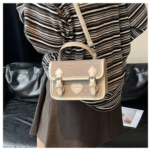 Detail of vintage beige messenger bag featuring heart patch and faux leather trim