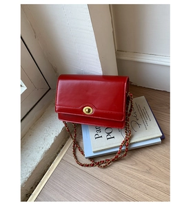 Detail of red crossbody bag featuring gold metal twist lock and woven chain strap