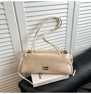 Détail d'un sac à épaule baguette beige avec logo métallique sur un canapé en cuir