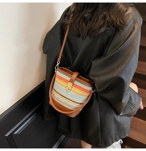Detail of multi-colored woven straw bucket bag with brown leather strap and gold buckle