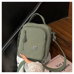 Detail of green nylon crossbody bag with multi-zipper layers and adjustable strap