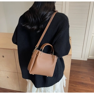 Close-up of brown litchi grain leather bucket bag featuring a metal top handle and logo