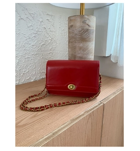 Detail of red leather crossbody bag featuring a vintage gold twist lock and chain strap