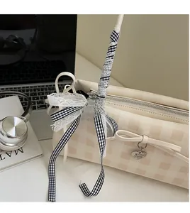 Detail of checkered beige handbag featuring a bow, heart pendant, and lace scarf handle
