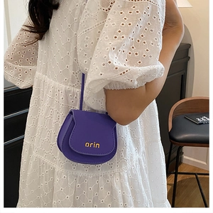 Detail of a purple leather mini saddle bag with gold logo paired with a lace dress