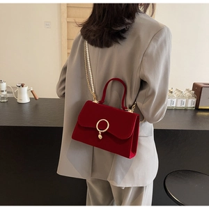 Detail of red velvet handbag with gold ring clasp and pearl chain worn over a grey blazer