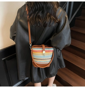 Detail of colorful woven straw bucket bag with brown leather strap and metal buckle closure