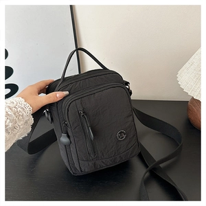 Close-up of lightweight black nylon crossbody bag with multi-pocket layers and metal logo