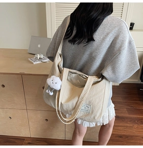 Détail du grand sac de voyage beige avec étiquette 'JUST YOUNG' et breloque nuage