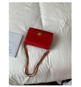 Detail of red glossy chain bag with golden swivel lock on white fabric background