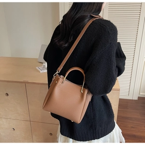 Brown lychee leather bucket bag styled on model with black sweater and white lace skirt