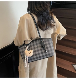 Close-up of a checkered leather tote bag with a plush bear charm on a trench coat