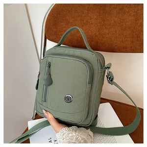 Detail view of a multi-compartment green nylon crossbody bag on a corduroy chair