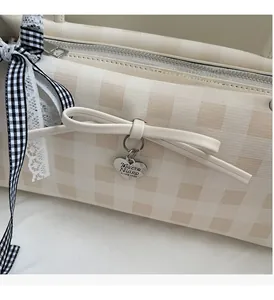 Detail of cream plaid shoulder bag with silver heart pendant and bow decoration