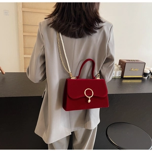 Close-up of wine red velvet handbag featuring a gold ring clasp and pearl chain strap