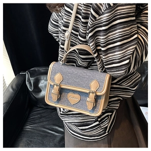 Detailed view of denim patchwork handbag featuring heart patch and metal buckle clasp