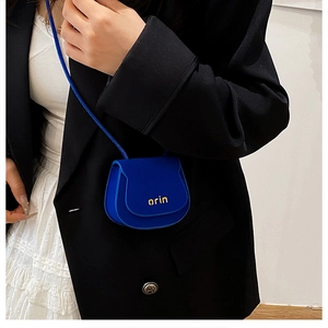 Close-up of a mini blue saddle bag with orin text worn over a black blazer and dress