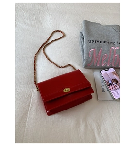 Flat lay of a red leather chain bag with gold lock closure on a white textured cloth