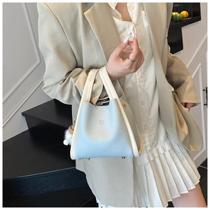 Detail of light blue bucket bag with pebble leather texture and fuzzy pompom charm