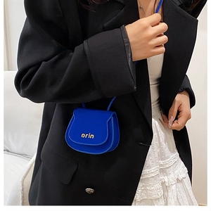 Close-up of minimalist mini saddle bag in electric blue worn with a black blazer